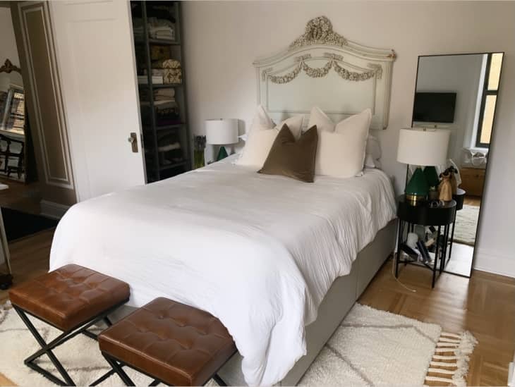 Warm bedroom with platform bed, antique plaster headboard, and two leather stools at the end of the bed