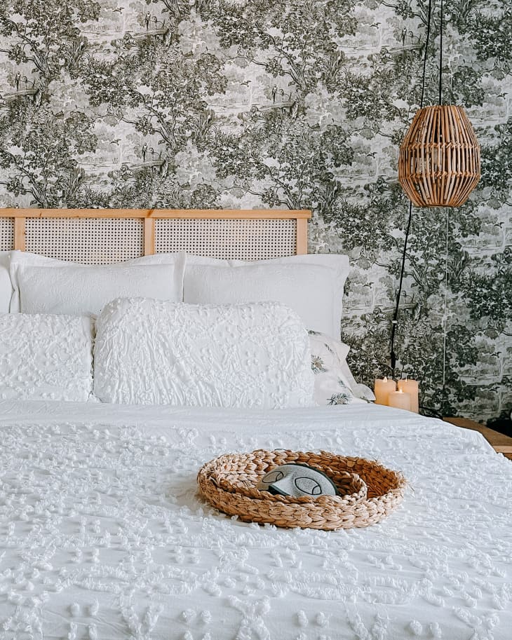 Bedroom with toile wallpaper, rattan lamp and headboard, and white bed linens