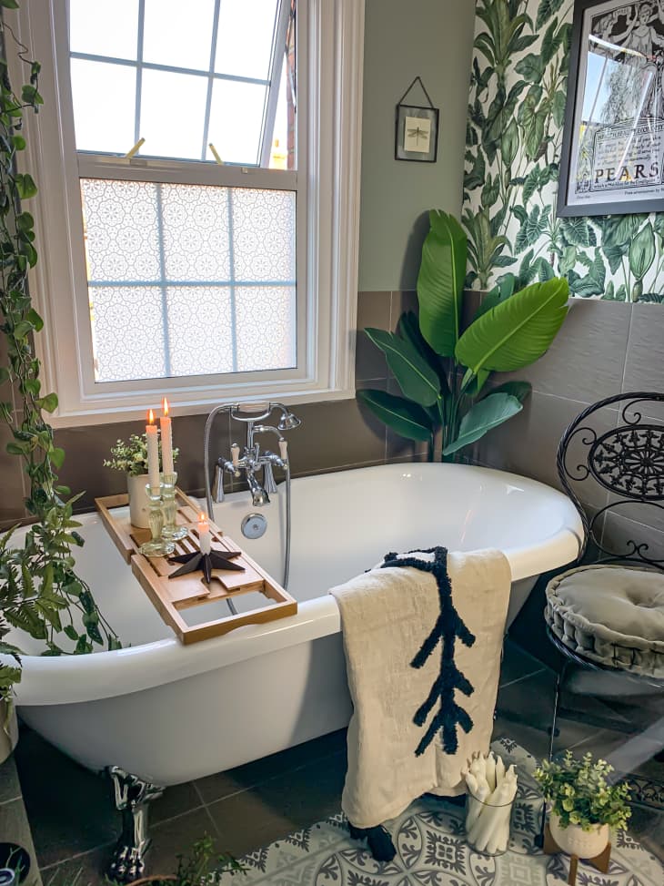 Clawfoot tub in bathroom with lots of plant and green and white tropical wallpaper