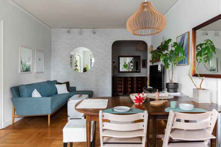 A small white living room with a blue sofa. A dining table separates the living space from the kids play area (not shown).