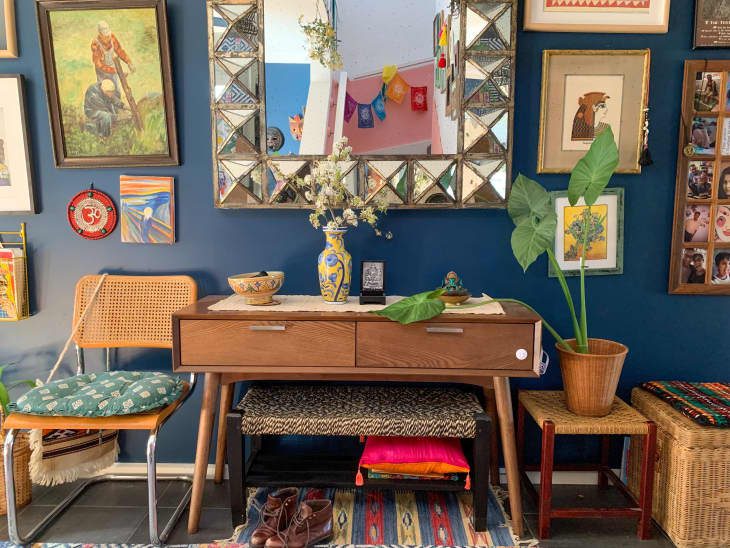 Mid-century style console table beneath mirror and other framed artwork in room with navy walls