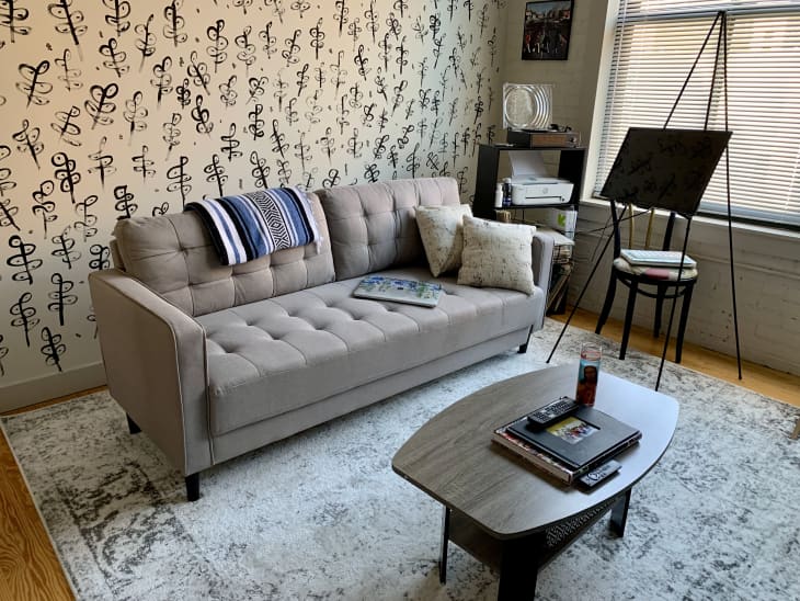 Living room with gray sofa, easel, and black and white hand painted mural behind sofa