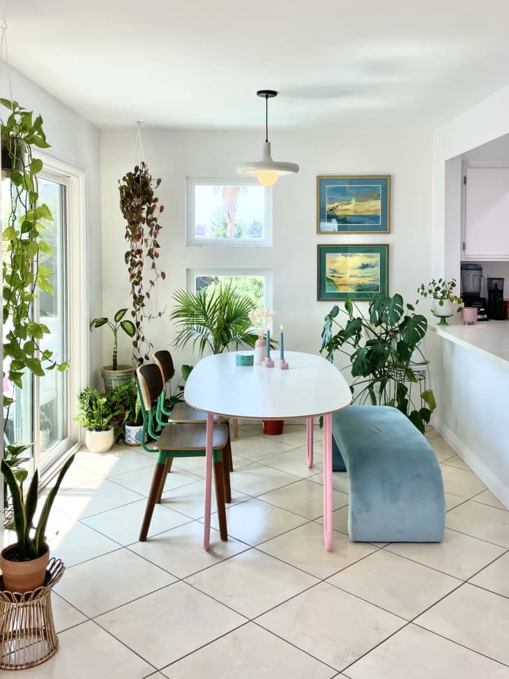 Plant-filled dining area with blue U-shaped velvet bench and table with pink legs