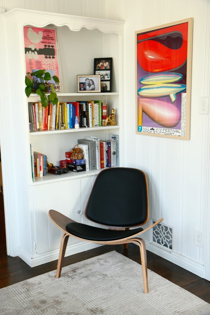 Black chair in corner next to colorful artwork and built-in shelf filled with books