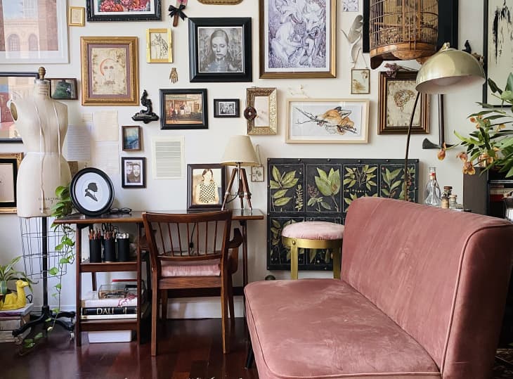 Pink loveseat and desk in room with gallery wall