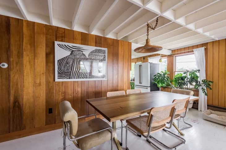 Wood-paneled dining area with large wooden table and cane Cesca chairs