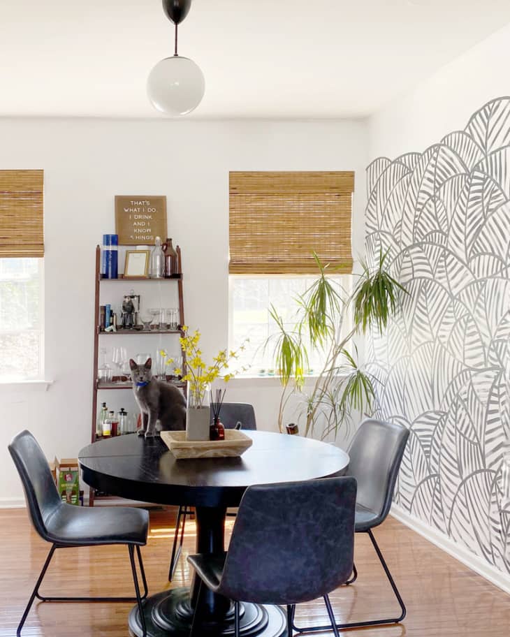 Dining room with round black table and palm leaf mural