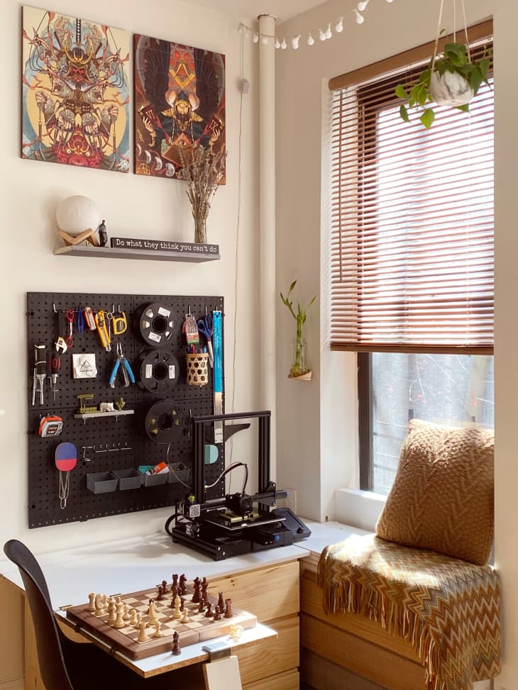 Sunny L-shaped desk corner with a window seat, a chess set, and a peg board on the wall with tools and supplies