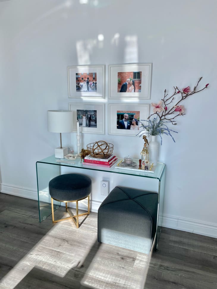 Acrylic console table with framed photos above and two stools beneath