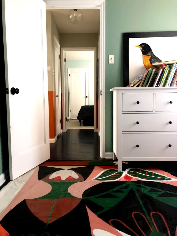 房间有绿色的墙壁，白色的梳妆台，鸟类艺术品和图形地毯