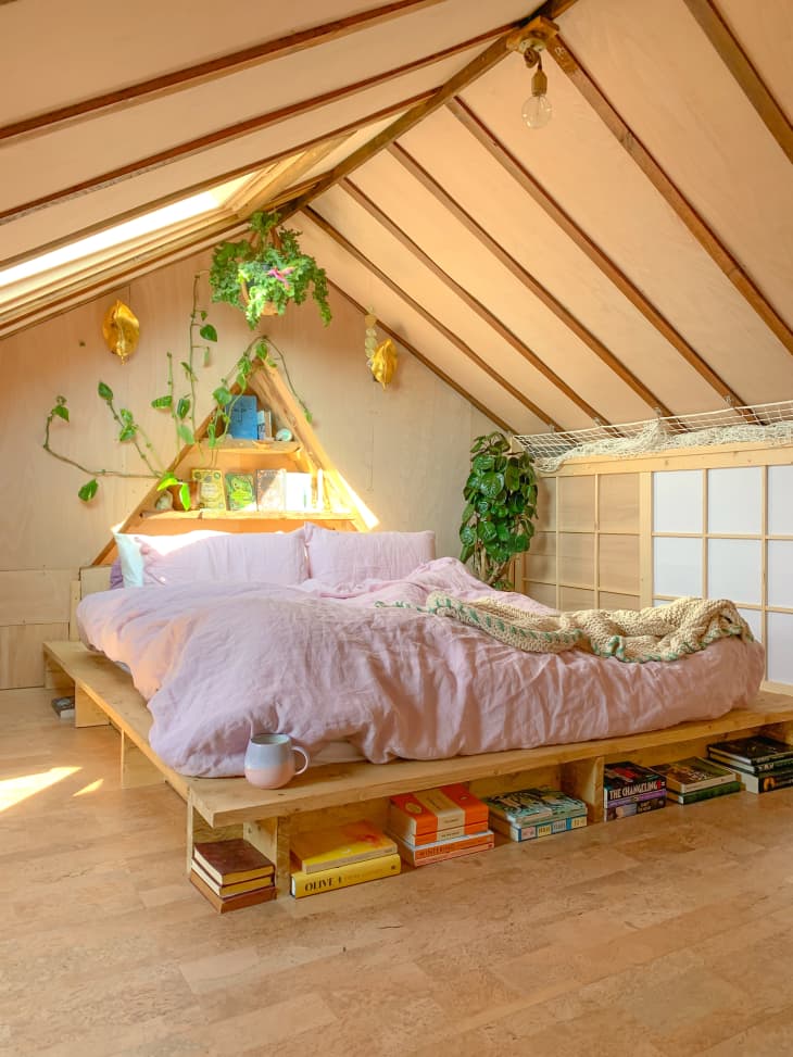 A-frame shaped all-wood attic bedroom with green plants and a bookshelf bed