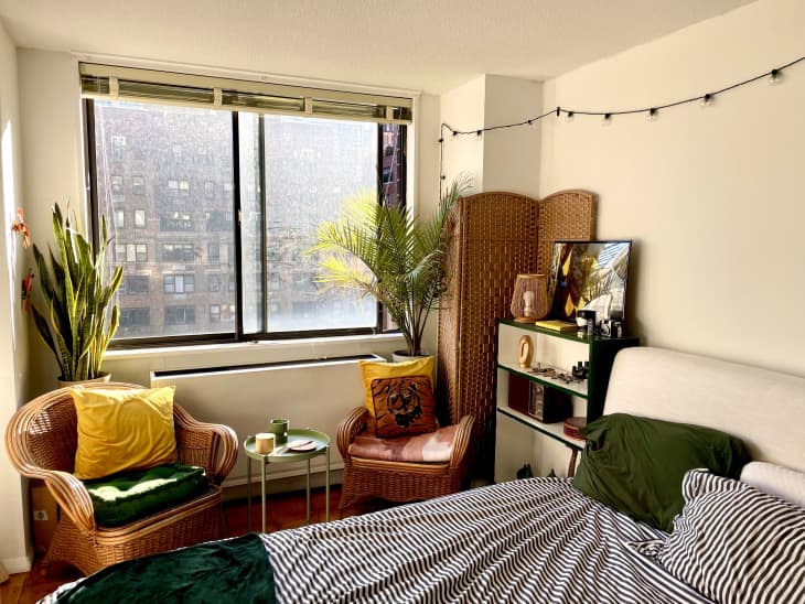 Bedroom with striped bed, wicker chair, and plants by window