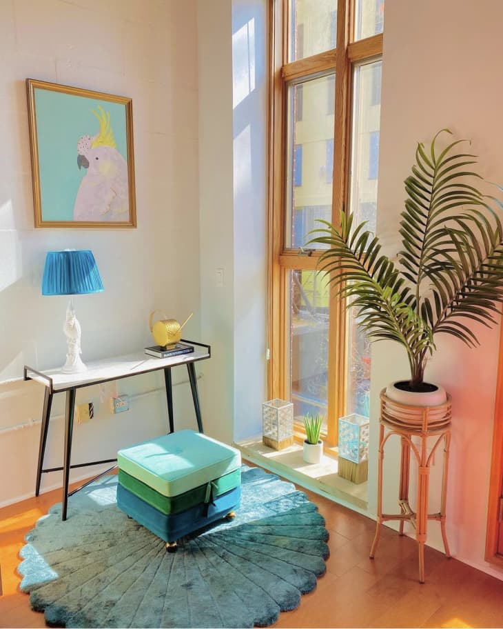 Corner of room by floor to ceiling windows with pastel colored art and a green plant