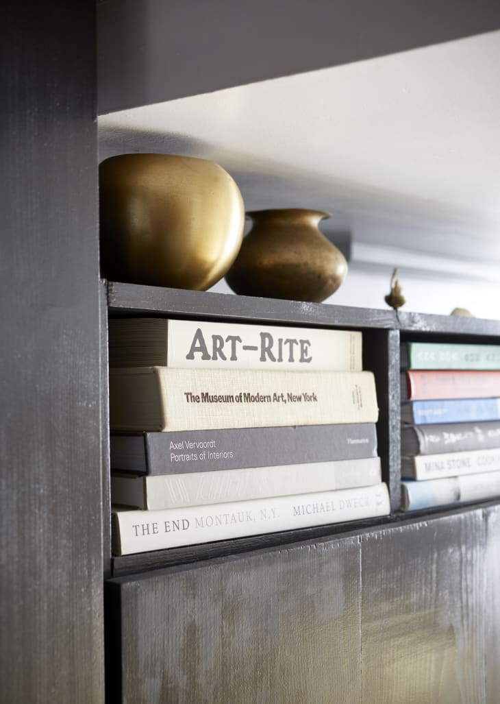 Close-up shot of art books stacked on a black cabinet with brass vases on top