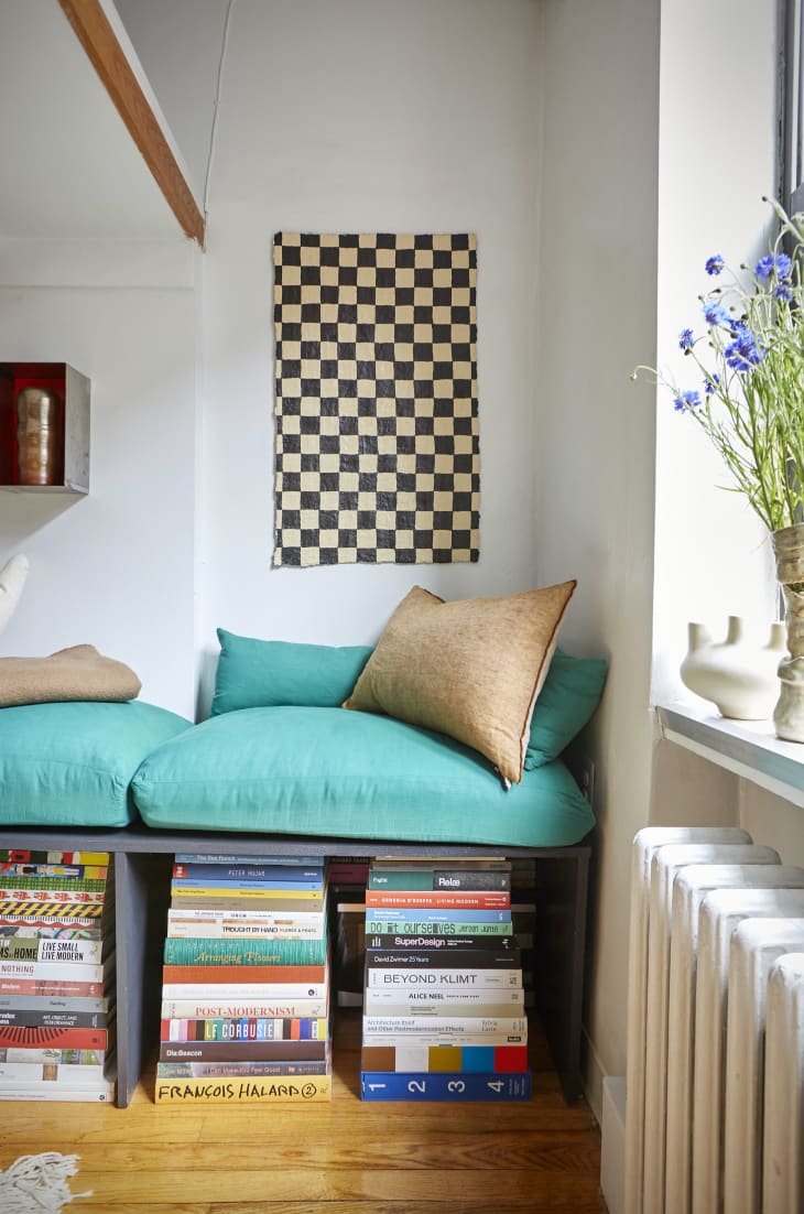 DIY sofa bench with teal cushions in pile of art books with plaid artwork hanging above