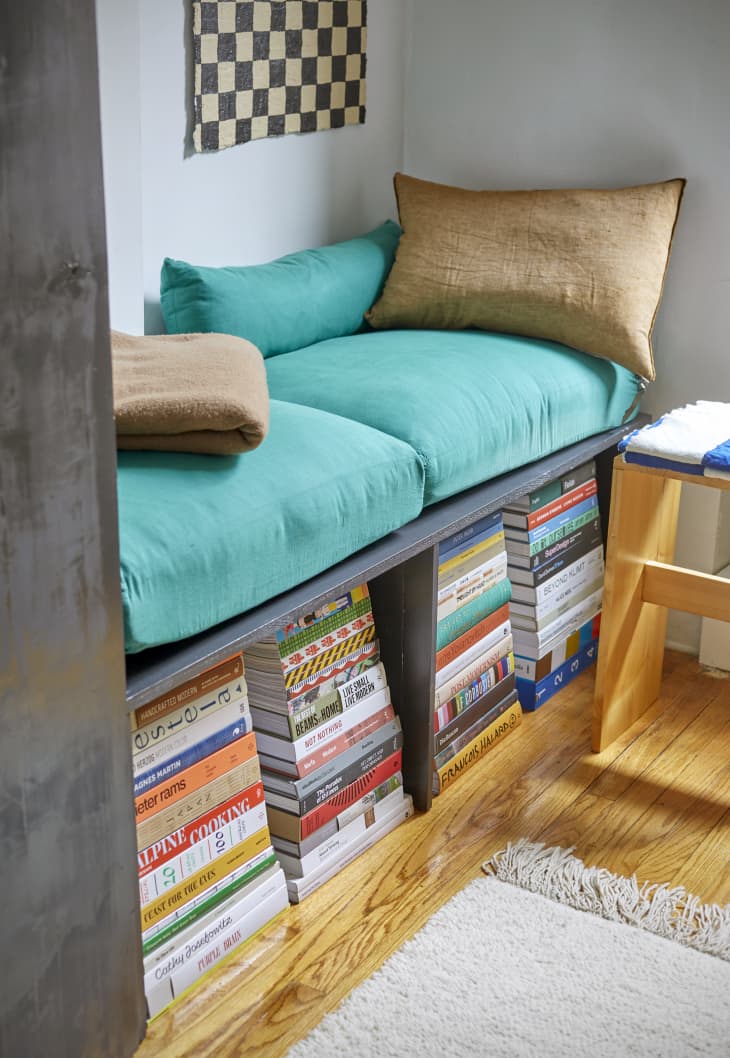 Close up shot of a DIY black wood sofa bench with book storage underneath and teal sofa cushions