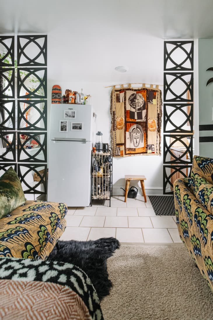 Eclectic living room with patterned sofas, a white fridge, and tribal wall art, separated by decorative black panels.
