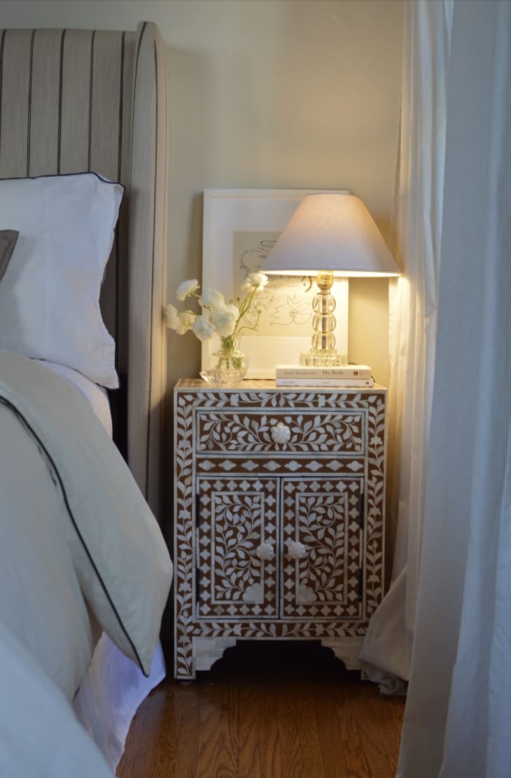 A patterned end table with a small lamp on top next to the bed