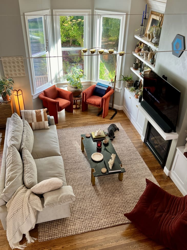 A bird's eye view of the living room with a white couch and orange chairs next to a large bay window