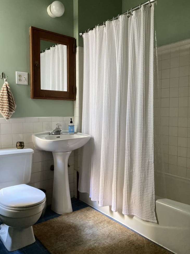 A green bathroom with white tiles and shower curtain