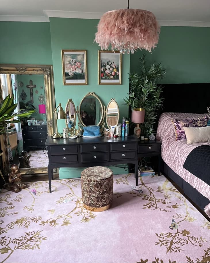 A green bedroom with a pink rug, bed, and overhead light
