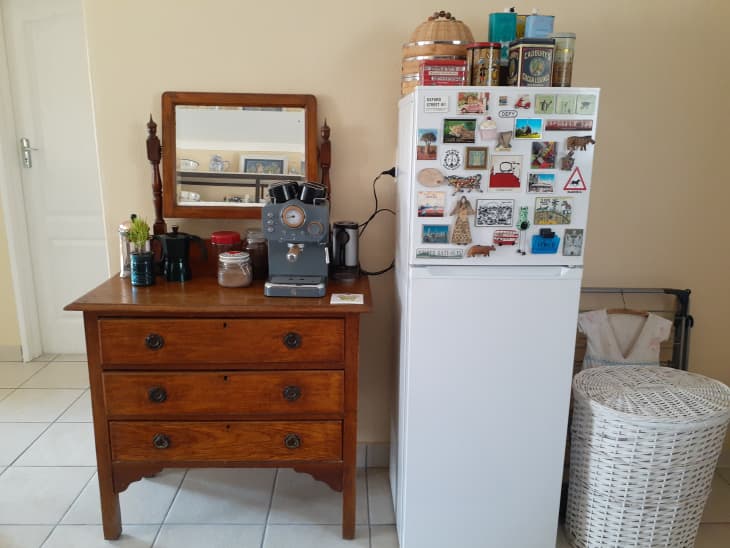 A brown wooden dresser next to a white refrigerator covered in photos