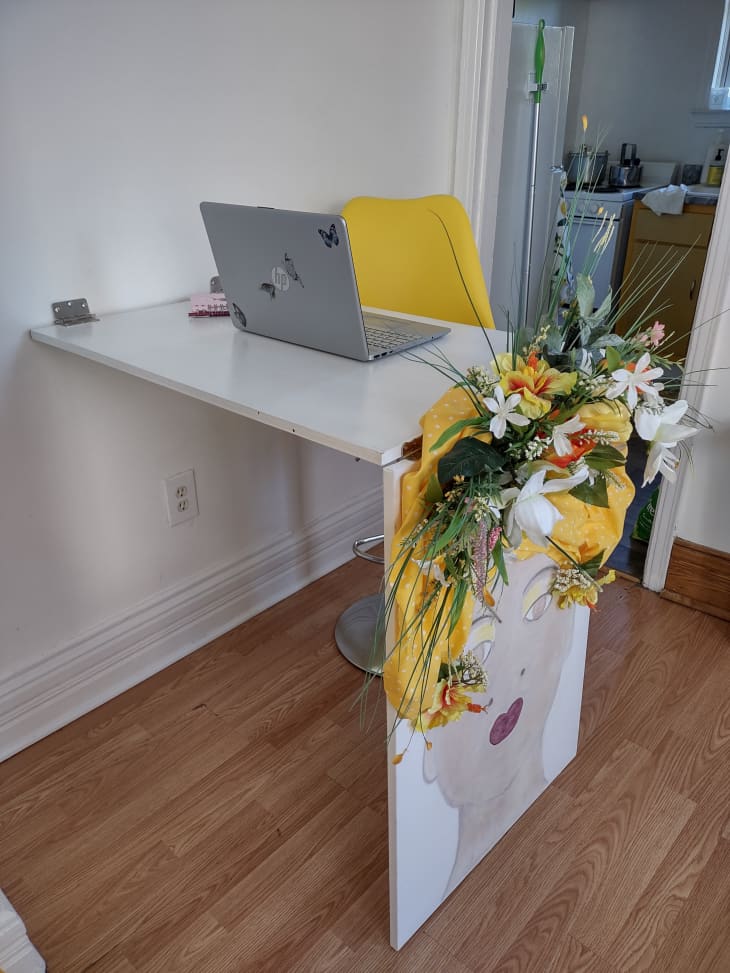 A desk with a laptop on top and a yellow bouquet on the side