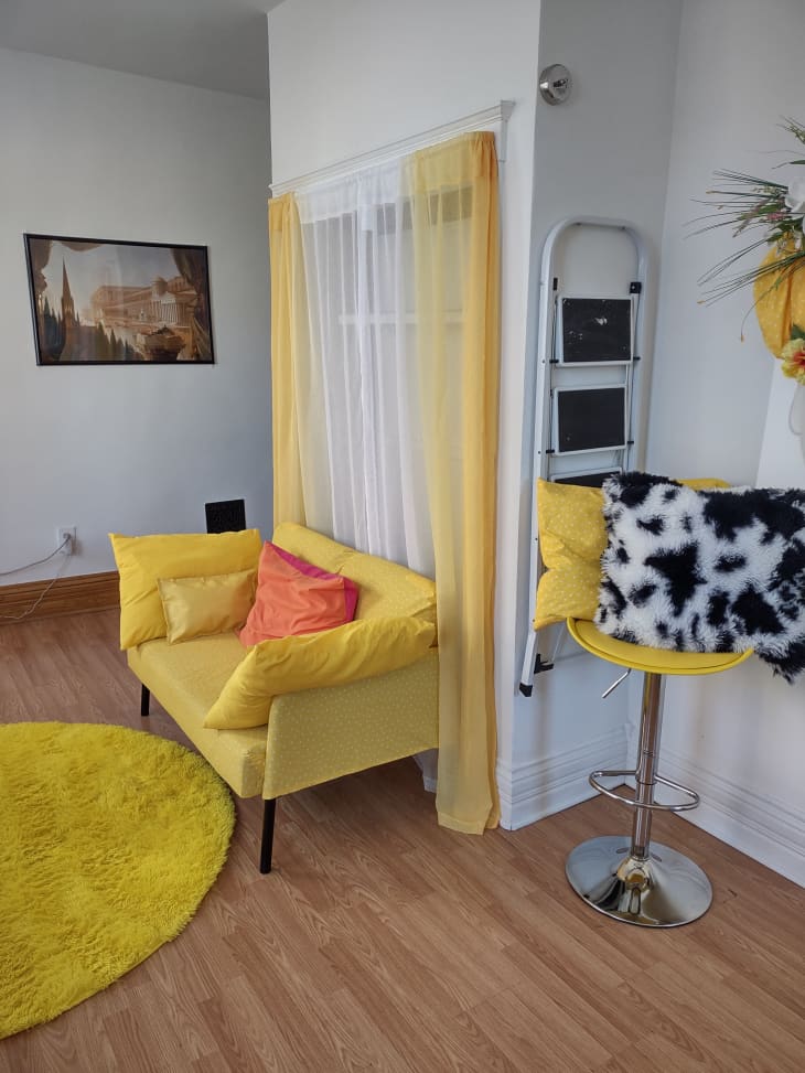 A small yellow sofa in front of curtains