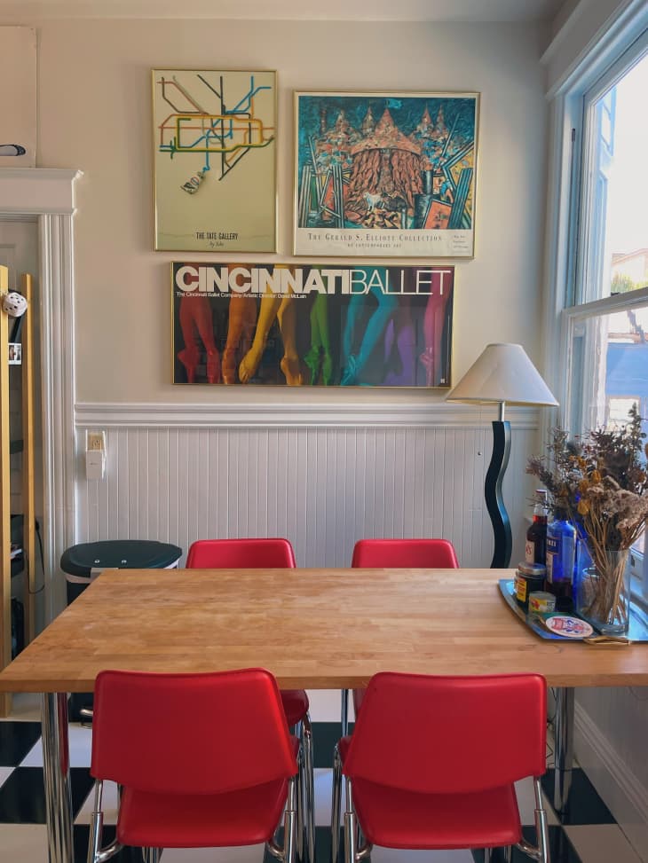 A kitchen with red chairs at a wooden dining table and art on the wall