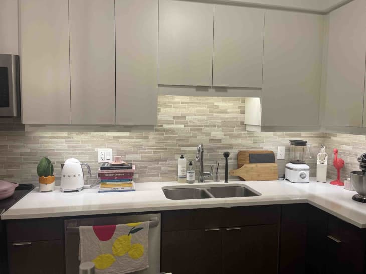 A modern kitchen with white counter tops and gray cabinets and a tiled backsplash