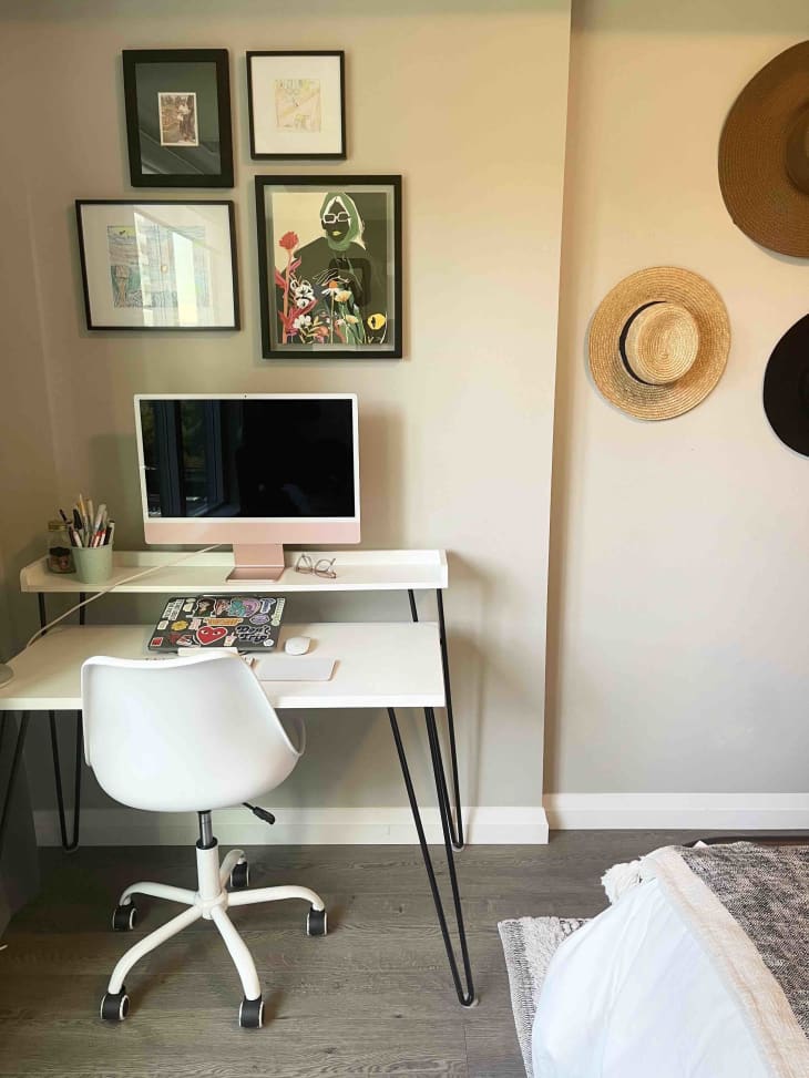 A white desk with a computer before four framed pieces of art on the wall