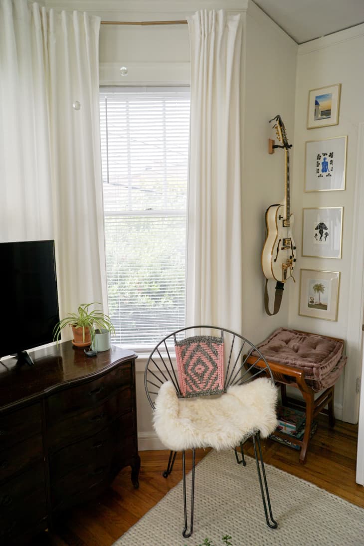 A chair with a faux fur cushion below a wall of art and a guitar
