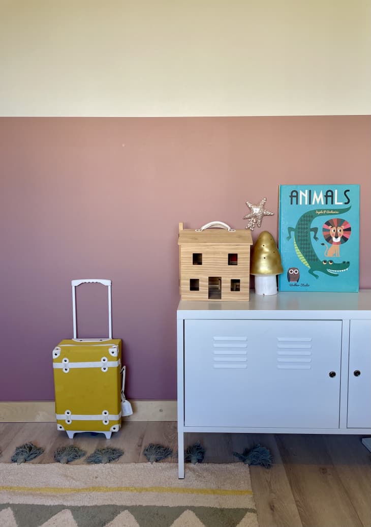 A room with pink walls and a yellow suitcase next to a white metal table