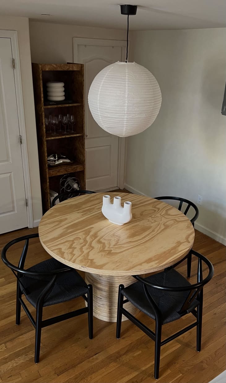 A round wooden dining table with four black chairs underneath a china ball