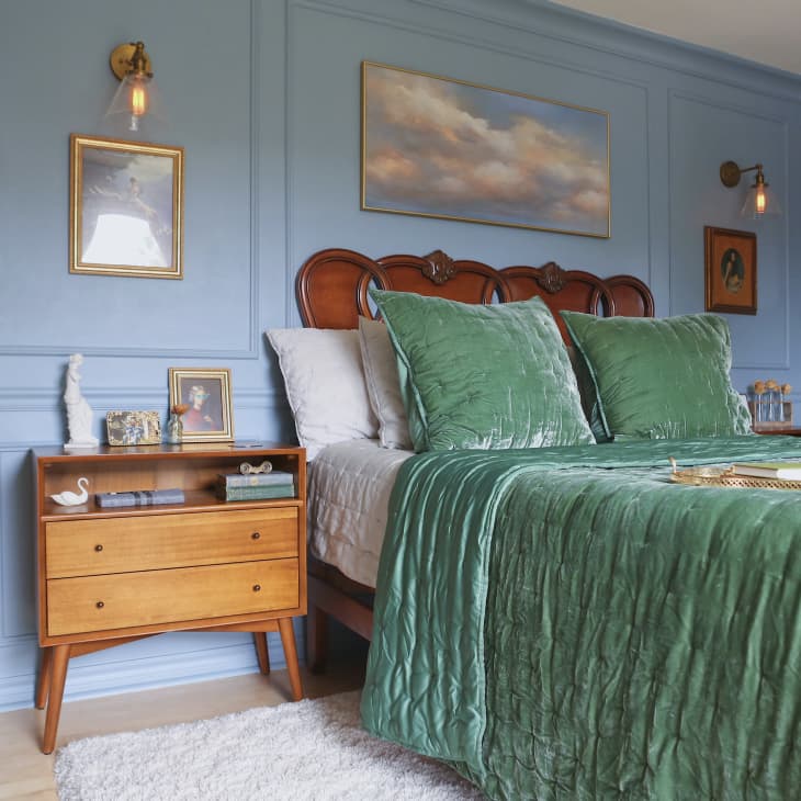 A blue bedroom with a wooden nightstand next to a queen bed with a teal velvet duvet