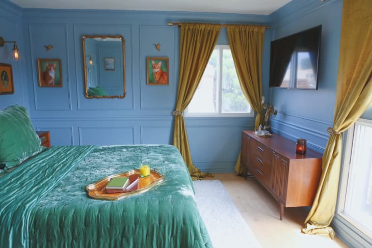 A blue bedroom with teal velvet blankets and yellow velvet curtains