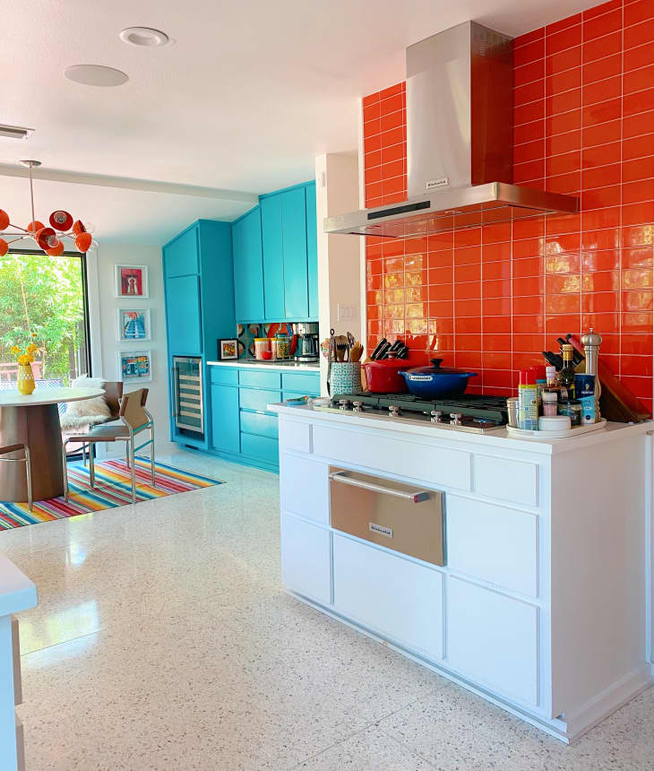 A kitchen with an orange tile splash and white and blue cabinets
