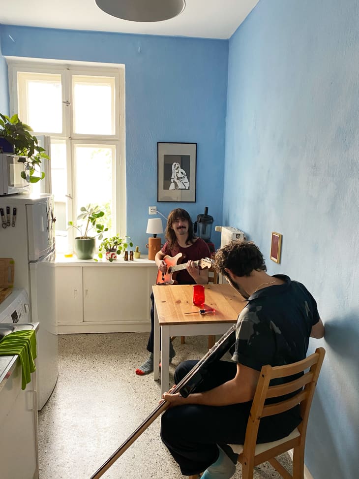 A blue kitchen with a table where two people are playing guitars
