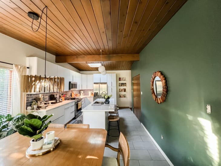 The view of the dining room and kitchen with wooden ceilings and a green accent wall