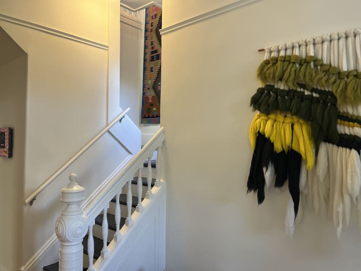 An entryway with a white staircase and woven art on the walls