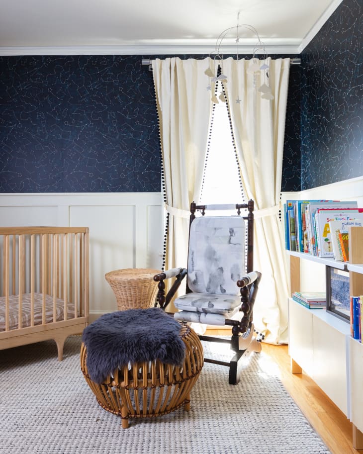 Dark blue baby nursery with white wainscoting and cream curtains with blue pom poms.