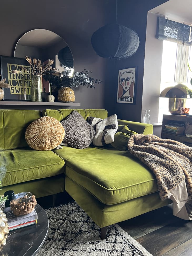 living room with gray walls, green velvet sectional sofa, cream and white rug, beaded chandelier, plants, art objects, cozy throw pillows and throw