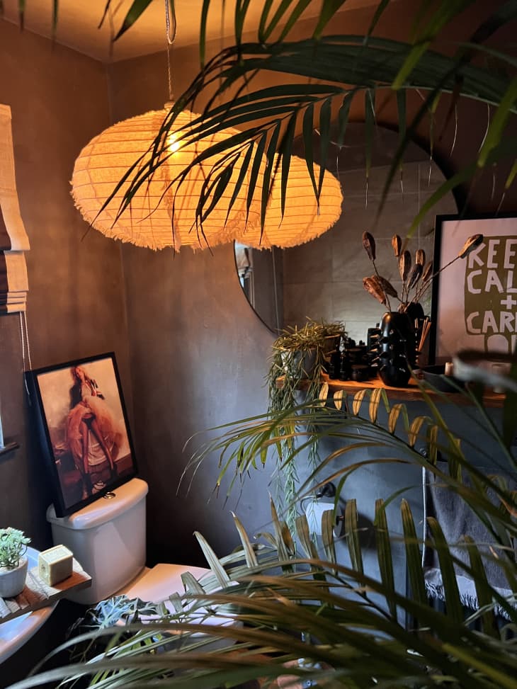 bathroom with gray walls, lots of large plants, paper lantern with very warm bulb/gold lighting, framed art