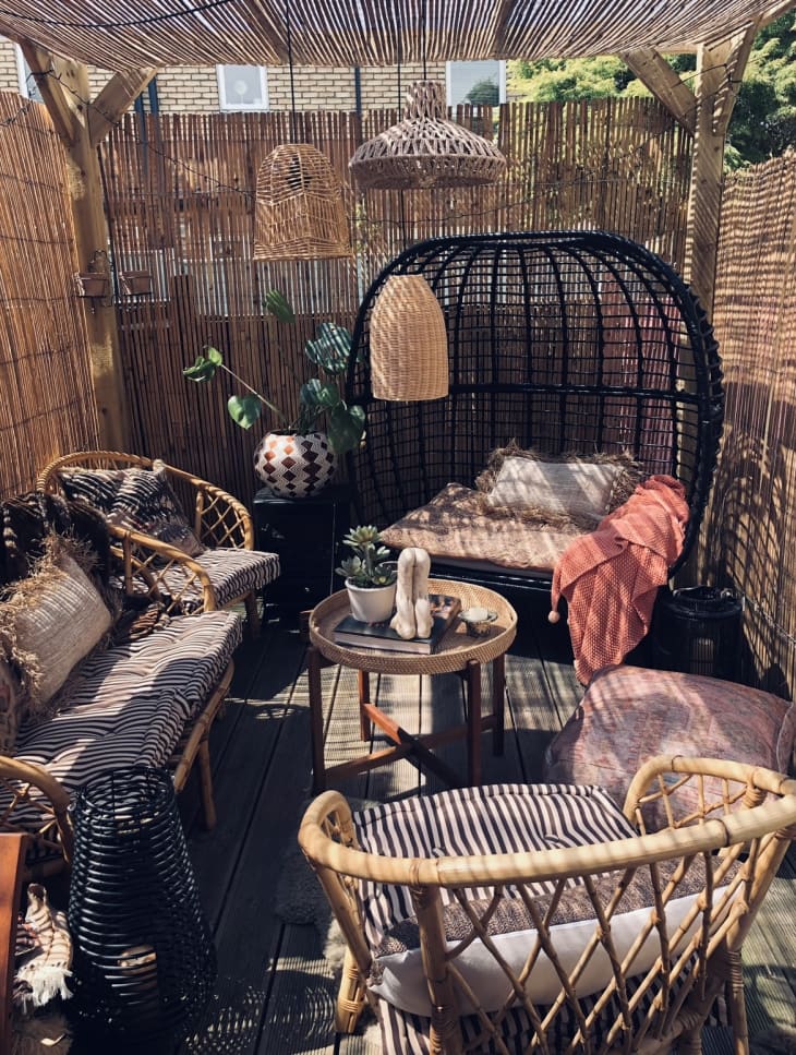 Outdoor patio with straw/cane/bamboo walls and "ceiling". Cane patio furniture (chairs, sofa, small round table), rattan hanging lamps