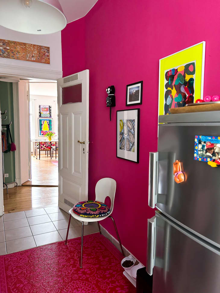 Hot pink kitchen with colorful wall art and stainless steel refrigerator.