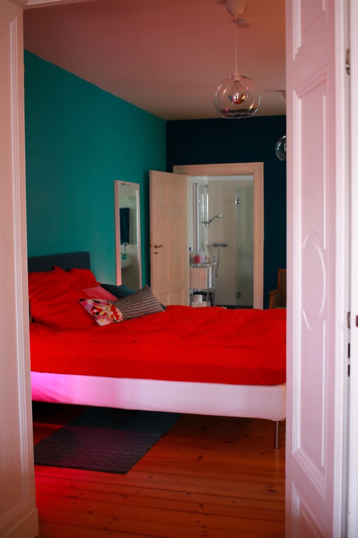 Colorful bedroom with red bed linens, aqua green walls and a single glass pendant on the ceiling.
