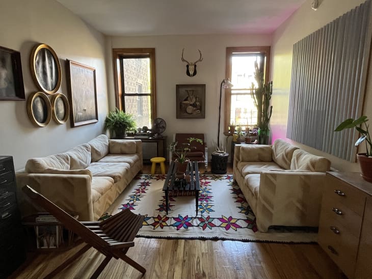 Living room with vintage beige/tan patterned sofa set flatweave colorful star pattern rug, slatted coffee table, plants, art