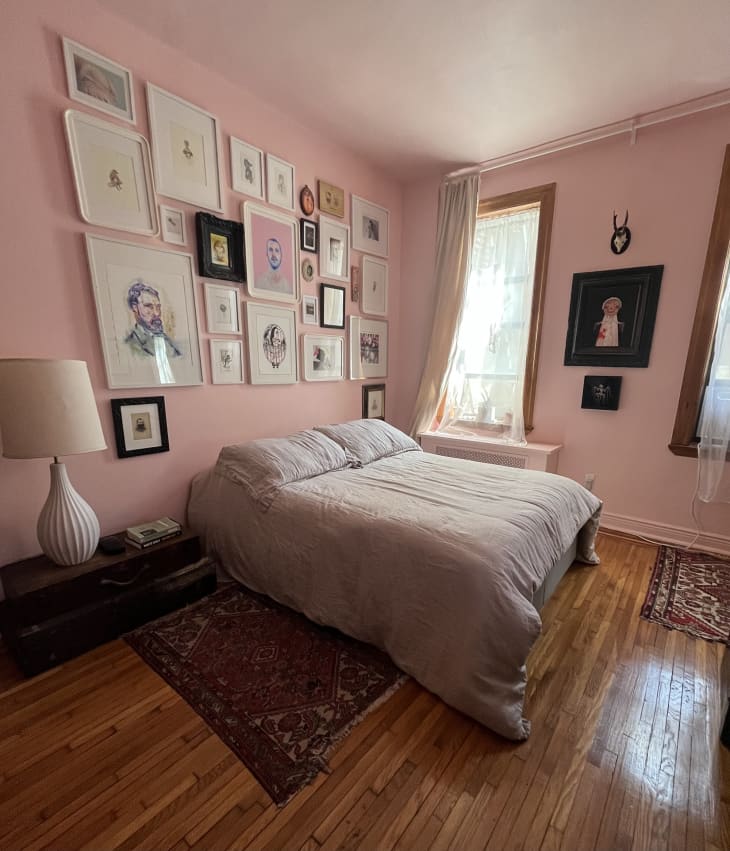 Bedroom with pink walls, gallery wall above bed, wood floors, 2 area rugs