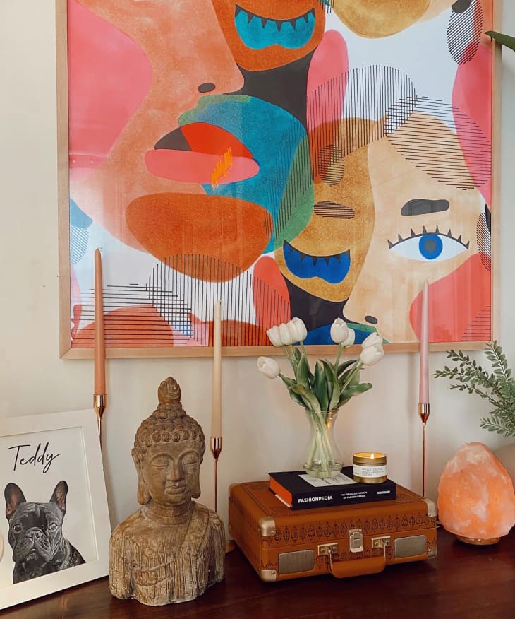 Credenza with alter featuring taper candles, Buddha's sculpture, and photo of french bulldog above a colorful painting.