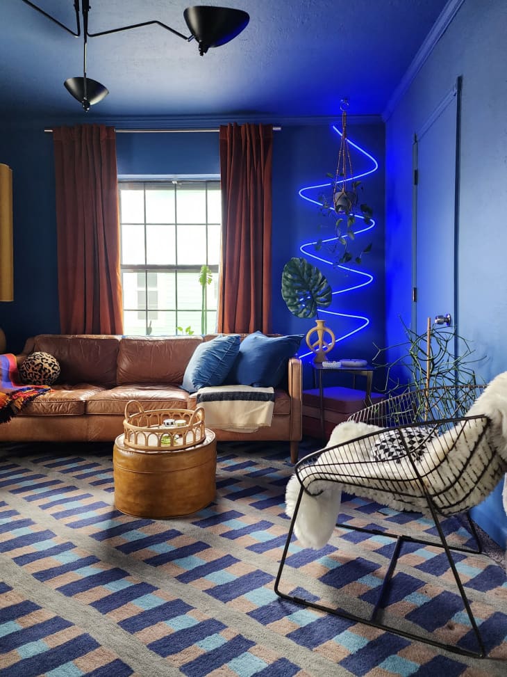 Living room with blue walls, blue neon art, leather sofa, geometric blue and gray rug